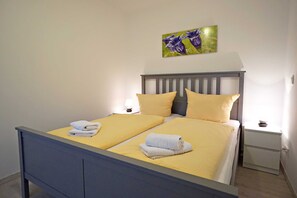 A double bed with two pillows, a bedside table, and a wall-mounted picture. - Apartment 5 ground floor - Vilma house (Heringsdorf)