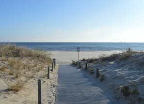 A wooden boardwalk leading to a beach with a signpost in the distance.