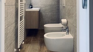 Un baño moderno con suelo de madera, un lavabo blanco, un bidé y un inodoro.
