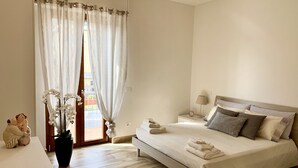 Un dormitorio con cama, mesita de noche, lámpara, planta en maceta y vistas al exterior.