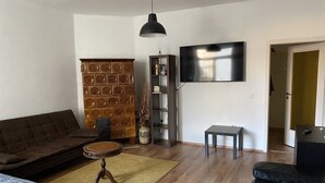 A living room with a brown sofa, a small round table, a bookshelf, and a flat-screen TV mounted on the wall. - Living in the historic imperial building (Wismar)