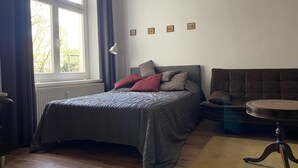 A bedroom with a bed, a chair, a table, and a window. - Living in the historic imperial building (Wismar)