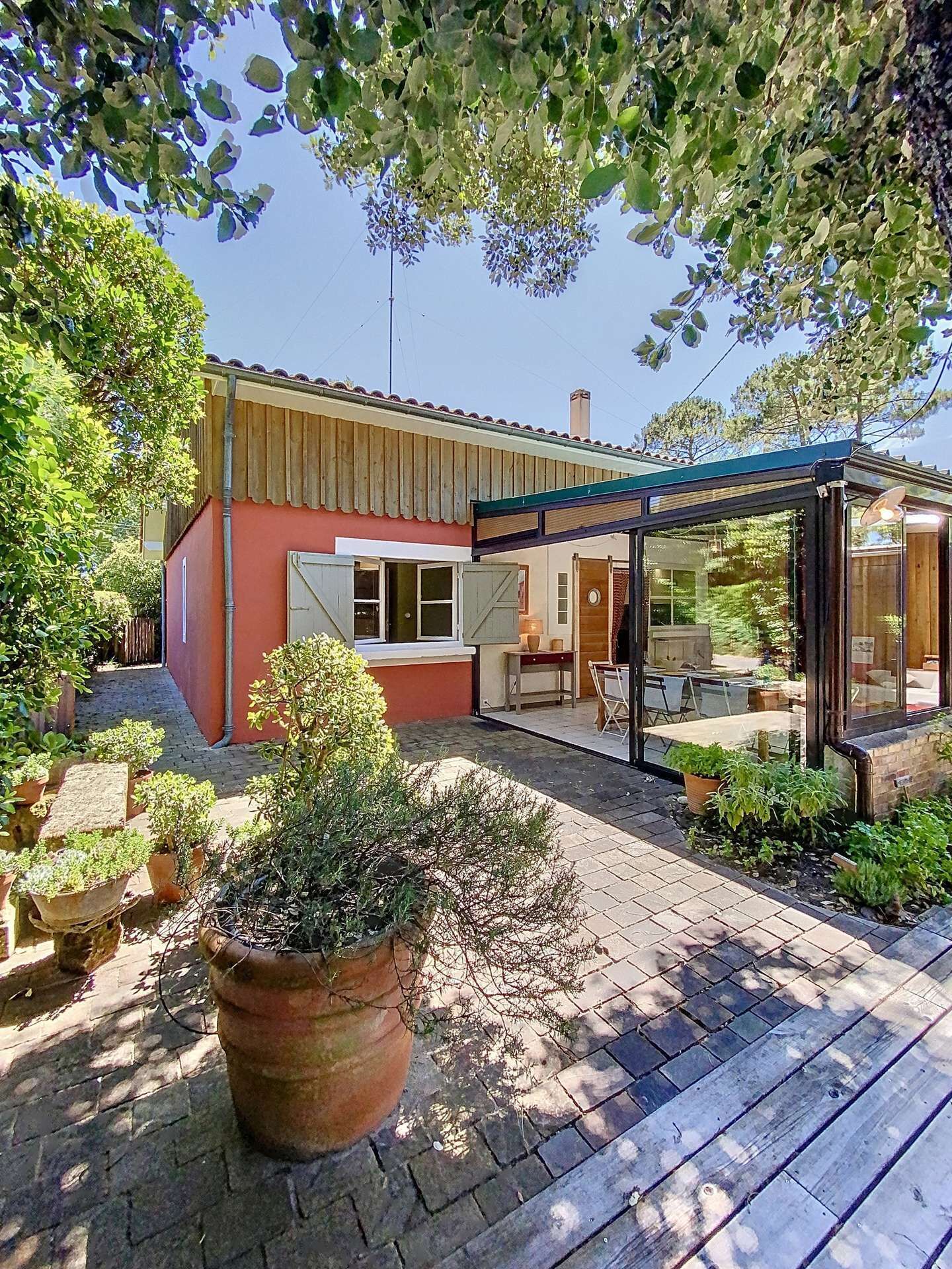 Ein Haus mit überdachter Terrasse, einem Pflasterweg und Kübelpflanzen.