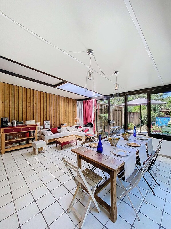 A modern interior with a dining area, wooden panel walls, and large windows offering a view of the outdoors. - Large House, 2 bedrooms and 1 mezzanine, 6 people, Longarisse, lake of Lacanau (LACANAU)