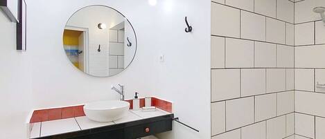 Ein modernes Badezimmer mit einem schwarz-weiß karierten Boden, einem weißen Waschbecken mit Spiegel darüber und einer Duschkabine mit weißen Fliesen.