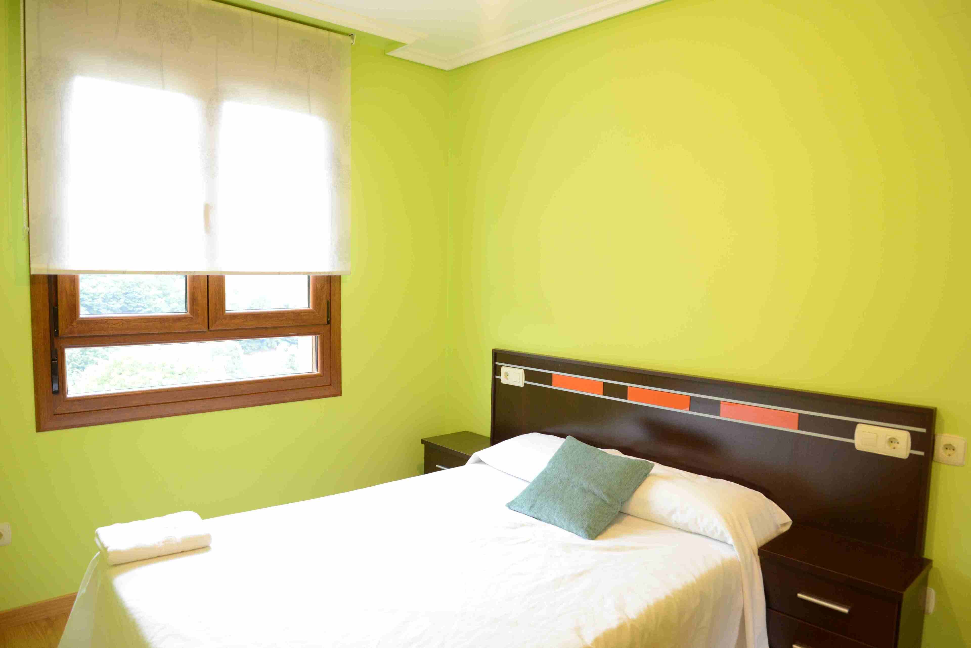 Een kamer met een bed, een nachtkastje, een raam met jaloezieën en een wand met een structuur.
