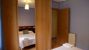Quarto de hotel com duas camas, portas de madeira, radiador e luminária no teto.