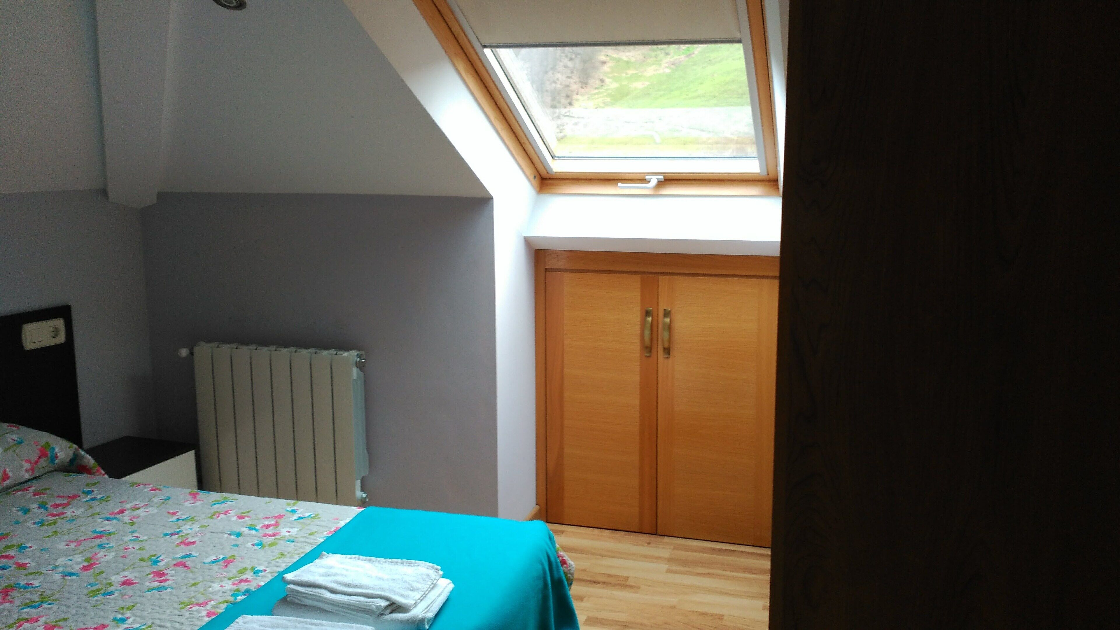 Un dormitorio con tragaluz, cama con cubrecama floral, radiador y armario de madera.