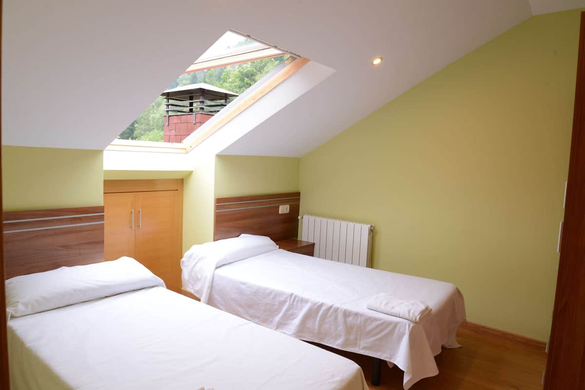 Quarto com duas camas, um claraboia, um guarda-roupa de madeira e um radiador.