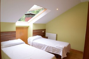 Una habitación con dos camas, un tragaluz, un armario de madera y un radiador.