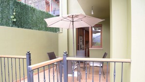 Uma varanda com mesa, cadeiras, grade de metal e um guarda-sol grande.