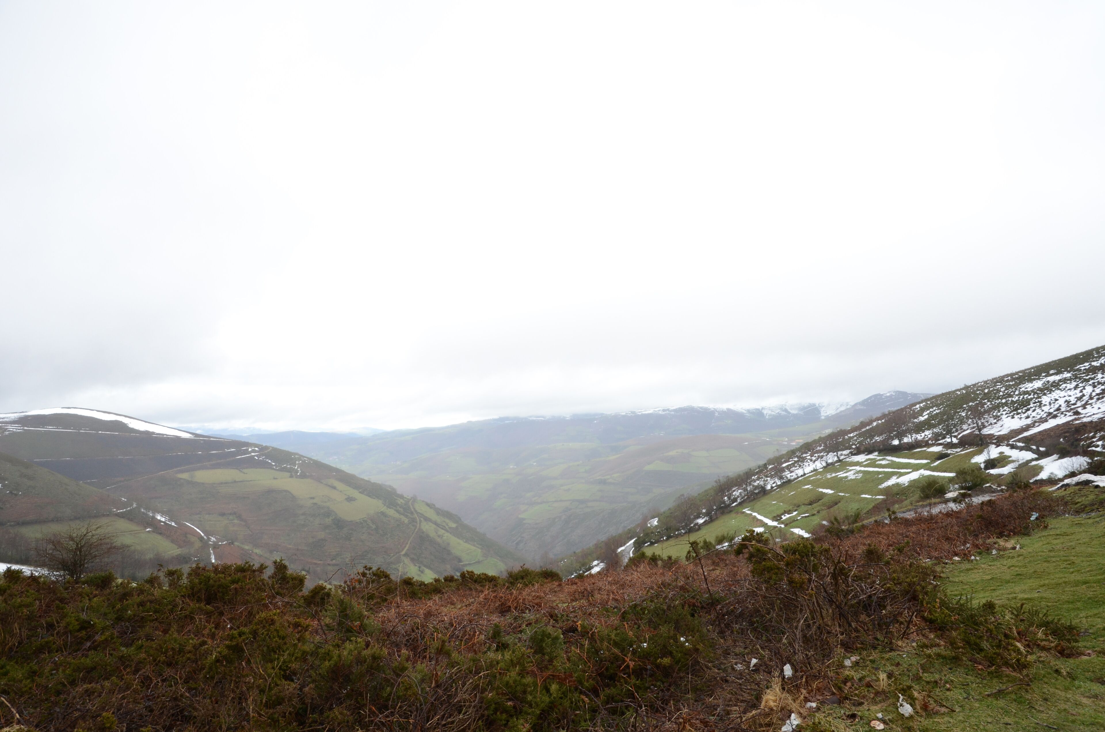 A mountainous landscape with a valley, some snow patches, and a few scattered buildings.