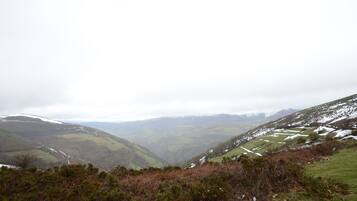 A mountainous landscape with a valley, some snow patches, and a few scattered buildings.