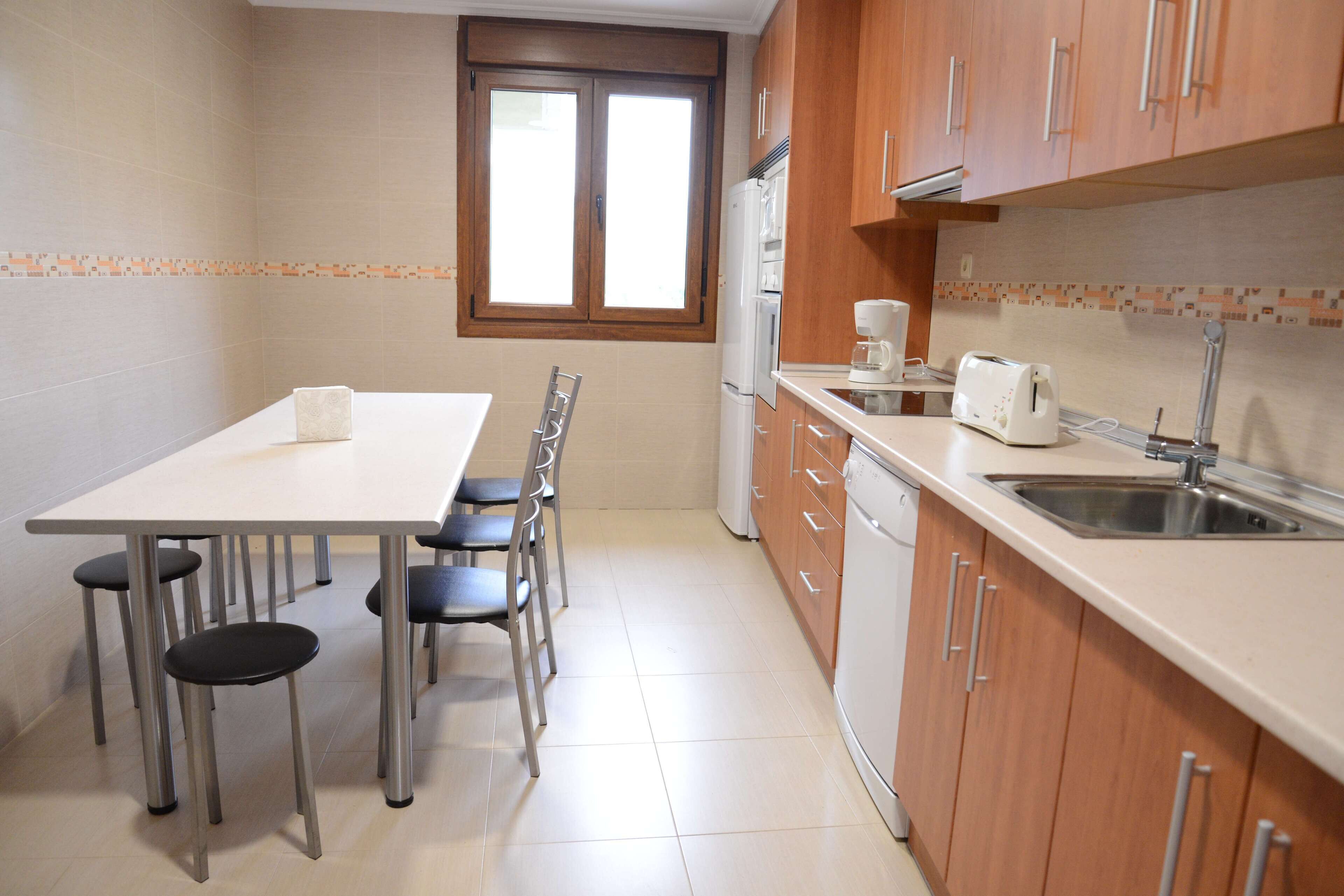 A kitchen with a dining table, chairs, a refrigerator, a coffee maker, and a sink.
