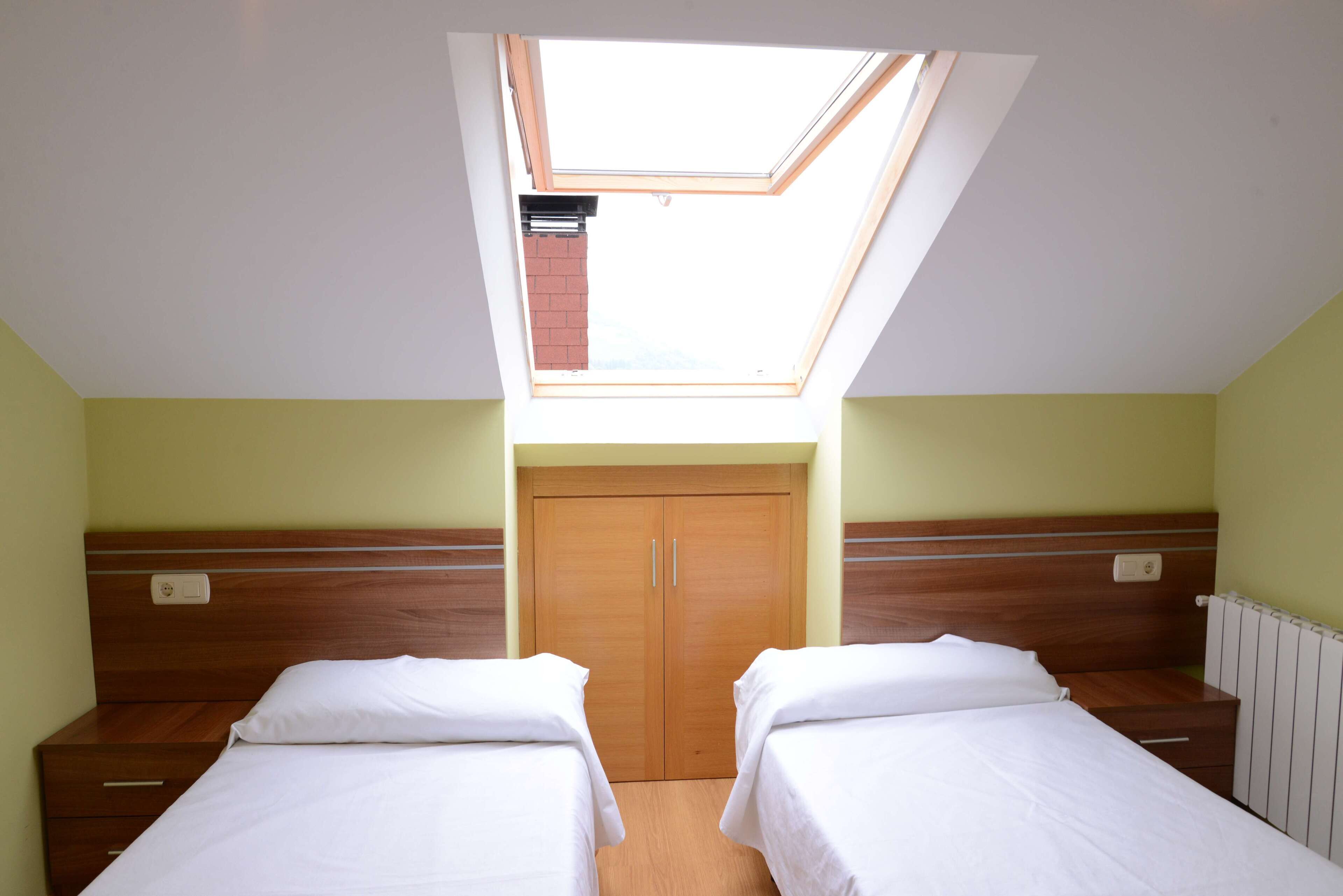 A room with two beds, a skylight, and a wooden wardrobe.