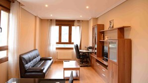Uma sala de estar moderna com um sofá de couro, uma mesa de centro de madeira, uma escrivaninha com uma cadeira e uma televisão sobre um aparador de madeira.