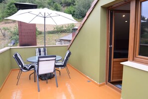 An outdoor patio with a table and chairs, a large umbrella, and a view of the surrounding landscape.