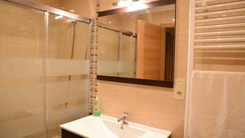 Une salle de bain avec une douche à parois de verre, un lavabo blanc et un miroir au-dessus.