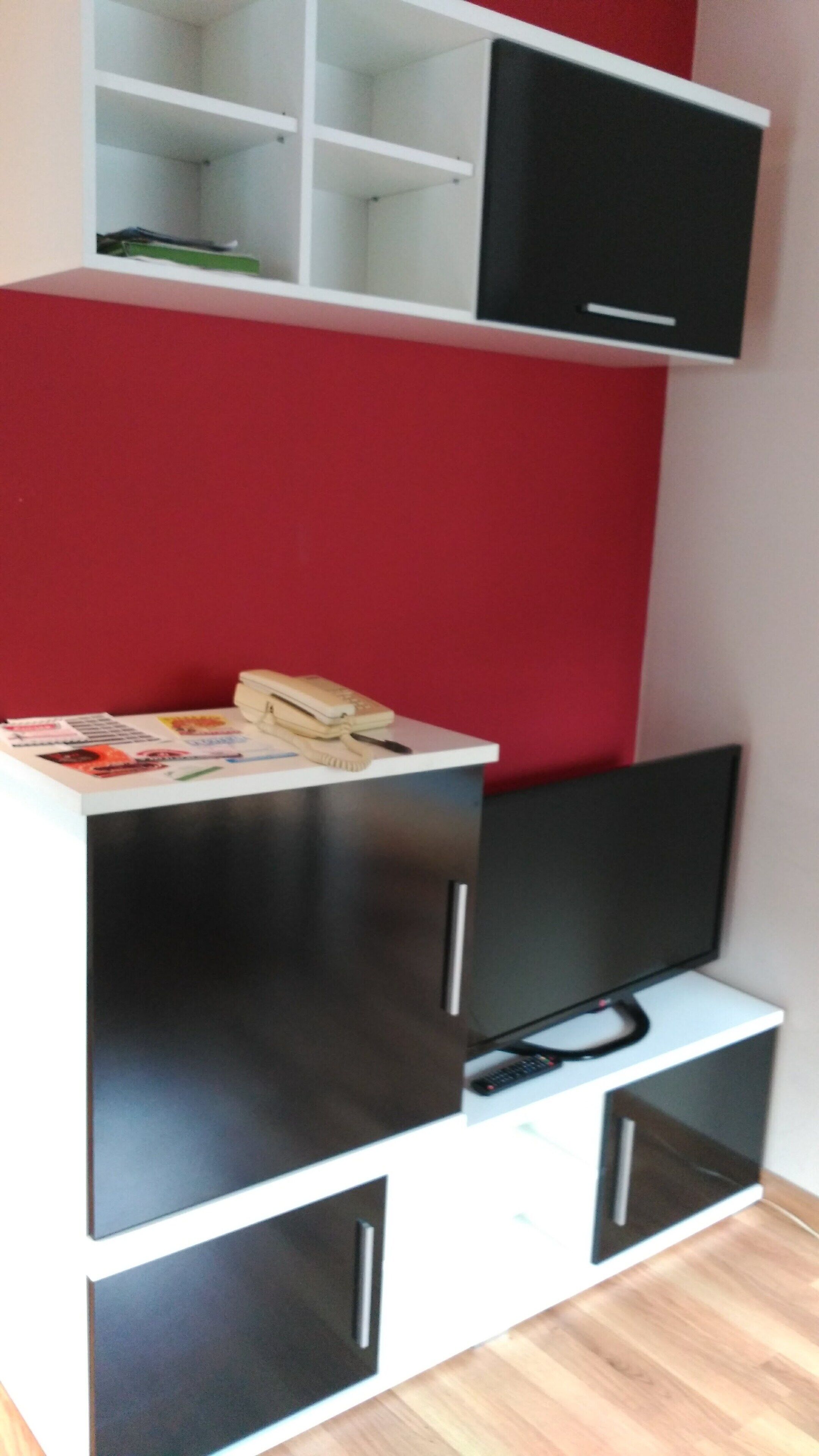 A room with a TV on a stand, a desk with a telephone and papers, and a red wall.