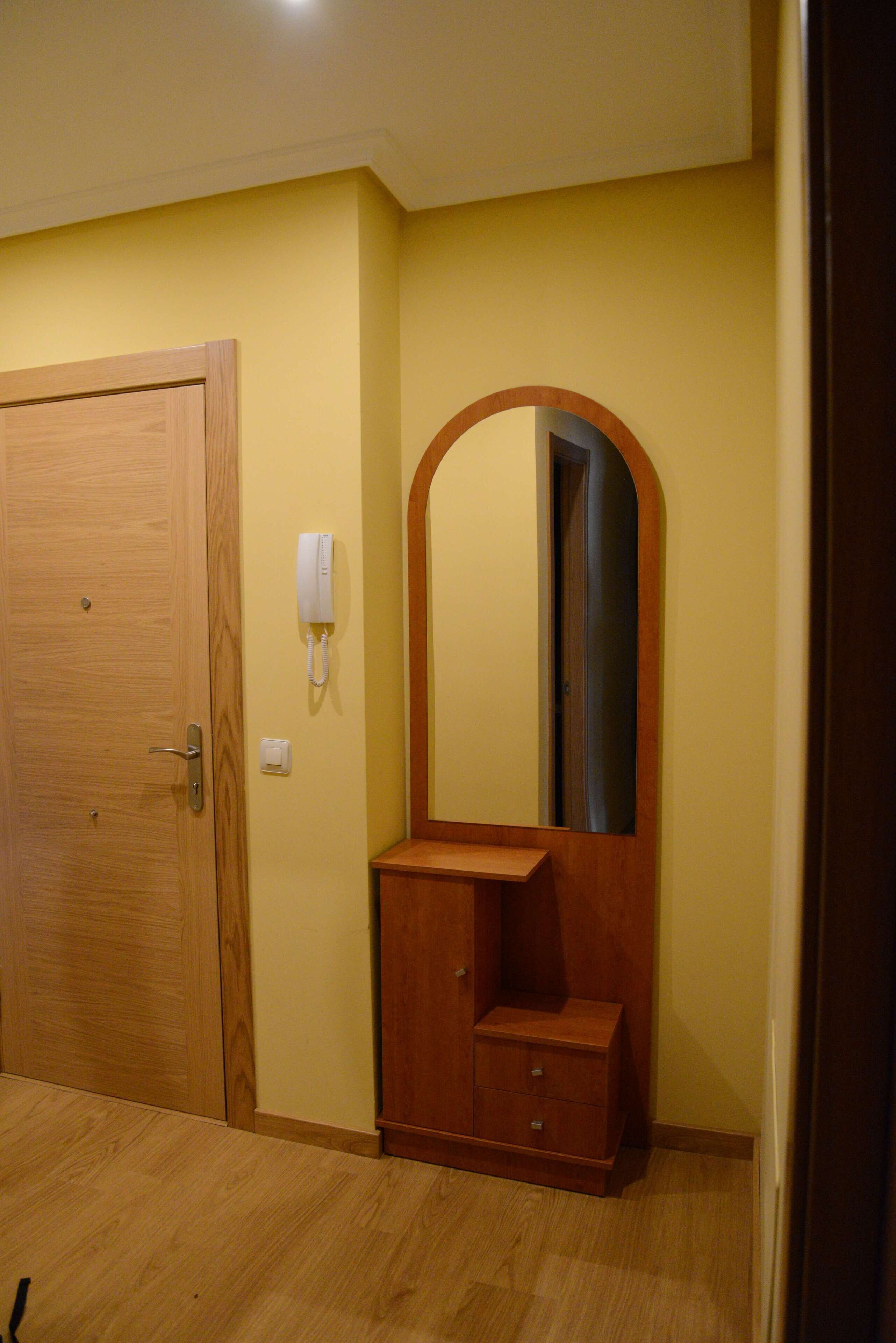 Una habitación con puerta de madera, un teléfono, un espejo y un mueble pequeño de madera.