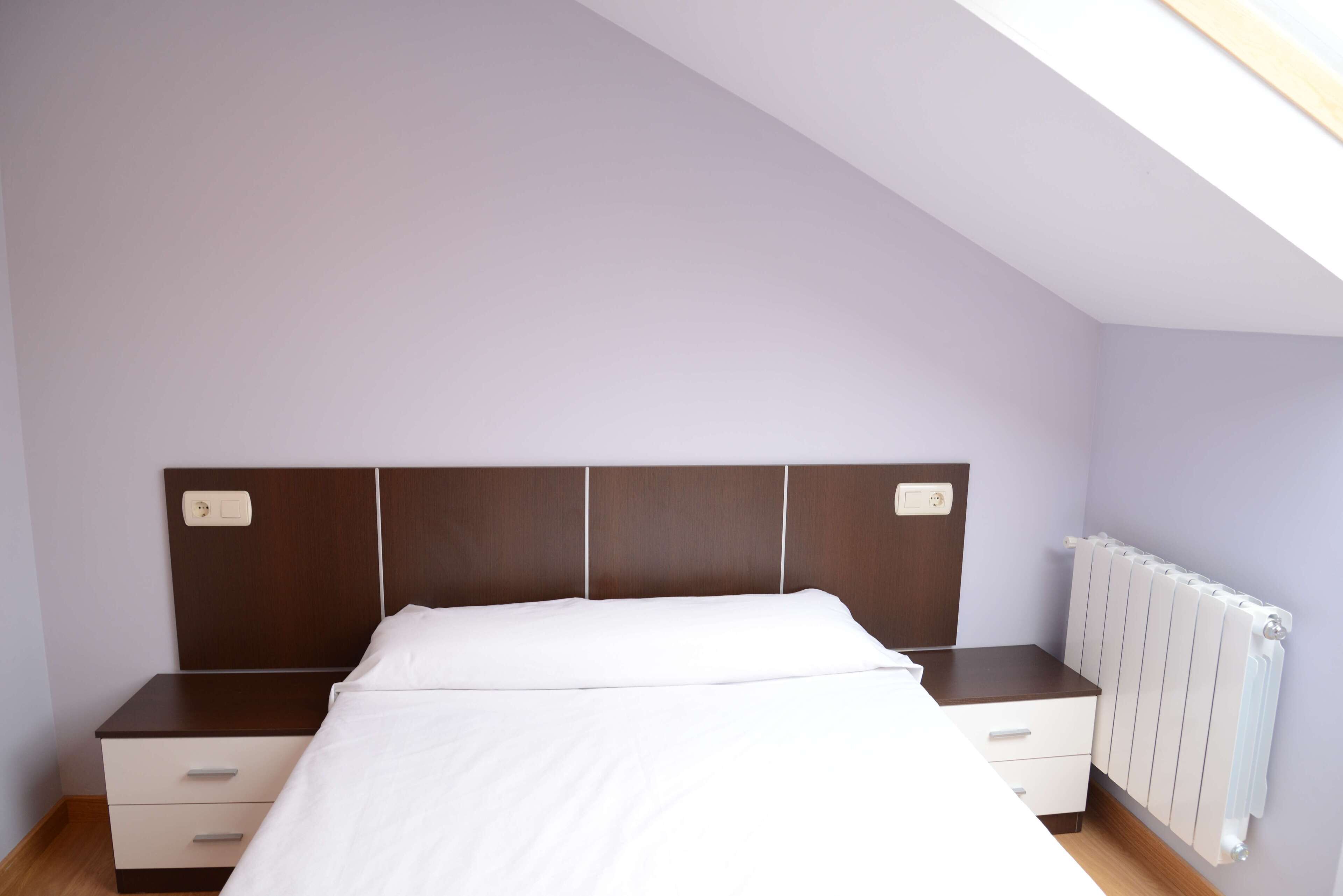 Ein Schlafzimmer mit Bett, Nachttisch, Kommode und Heizkörper.