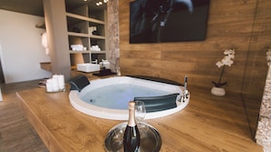 Une salle de spa équipée d’un jacuzzi, d’un plancher en bois, d’un téléviseur fixé au mur et d’une bouteille de champagne posée sur la table.