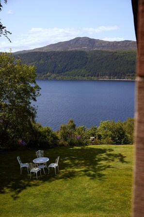 A grassy area with a table and chairs, overlooking a lake and forested mountains. - Foyers Lodge (Inverness)