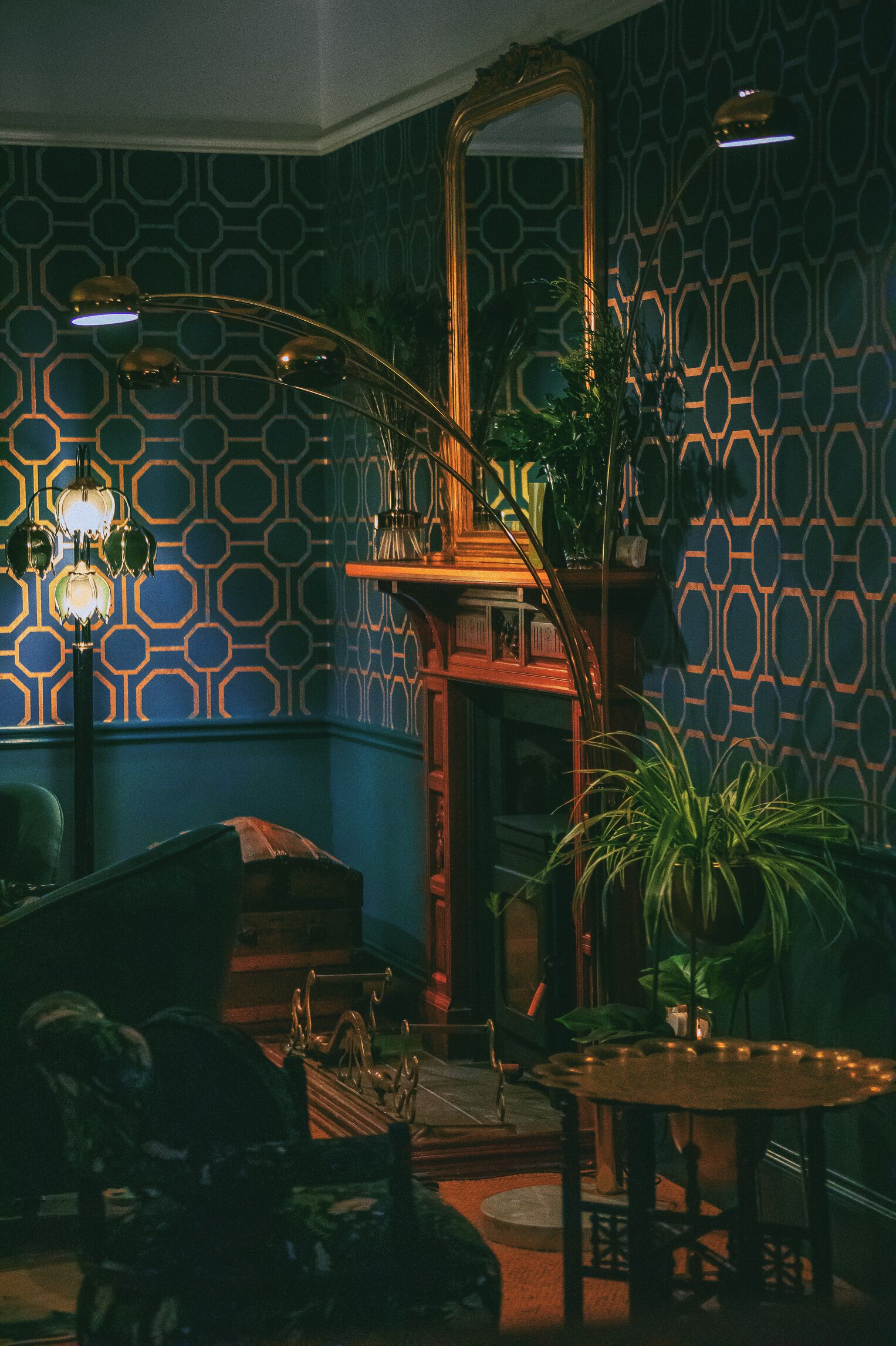 A room with patterned wallpaper, a large mirror, a staircase, and a dining table with chairs.