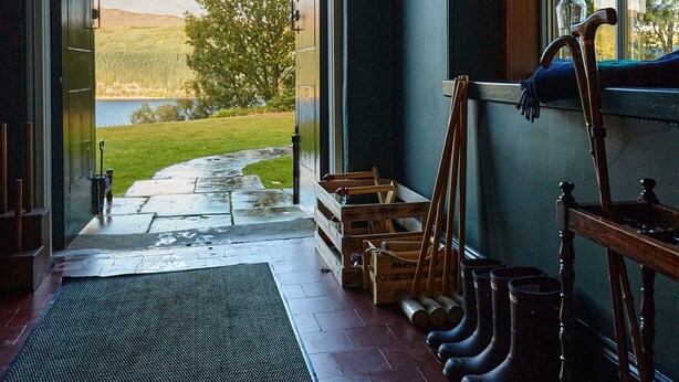 A room with a large arched doorway leading to a scenic outdoor view, a wooden bench, and a window with a vase of flowers. - Foyers Lodge (Inverness)