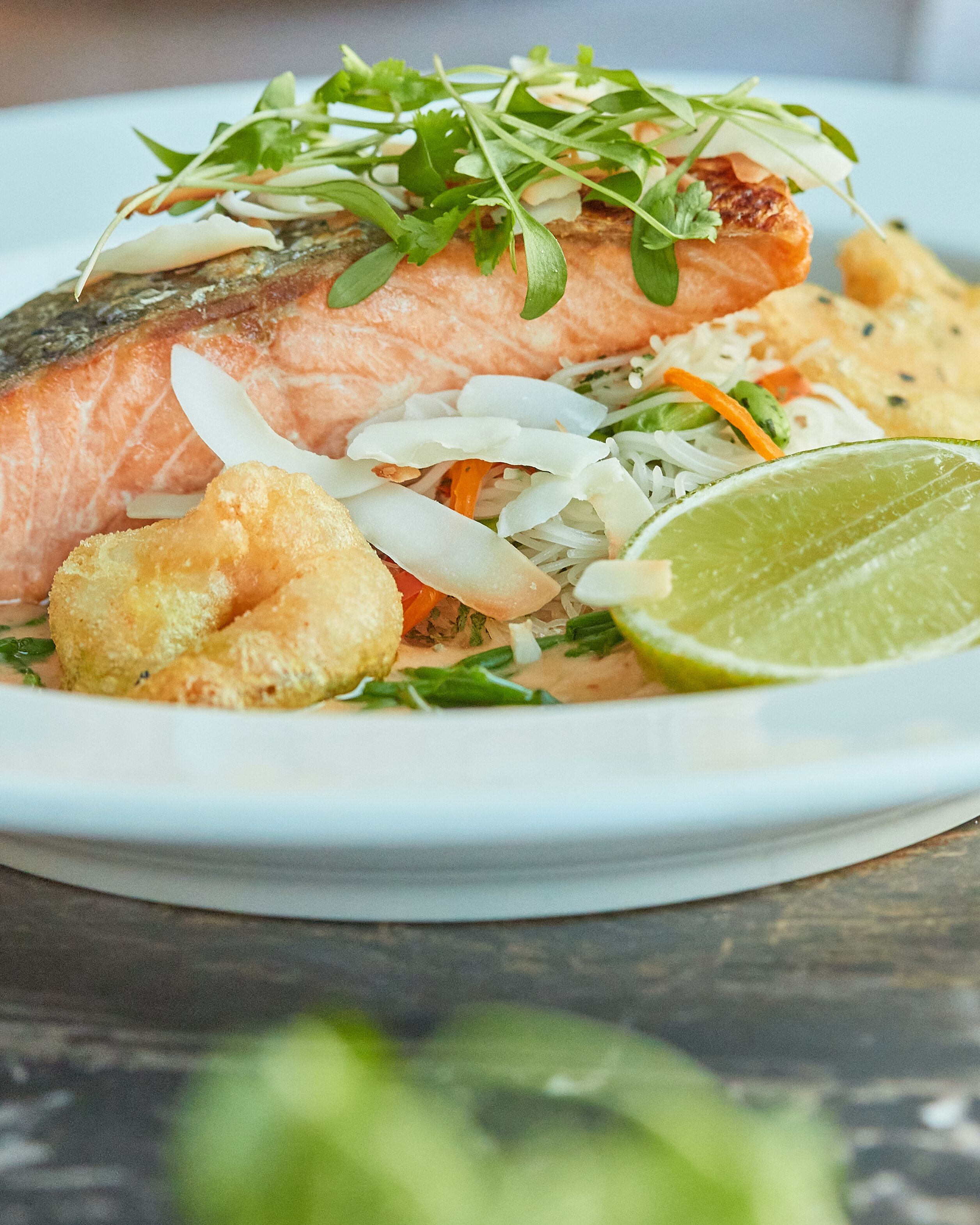 A plate with a piece of salmon, shredded vegetables, and a lime wedge.