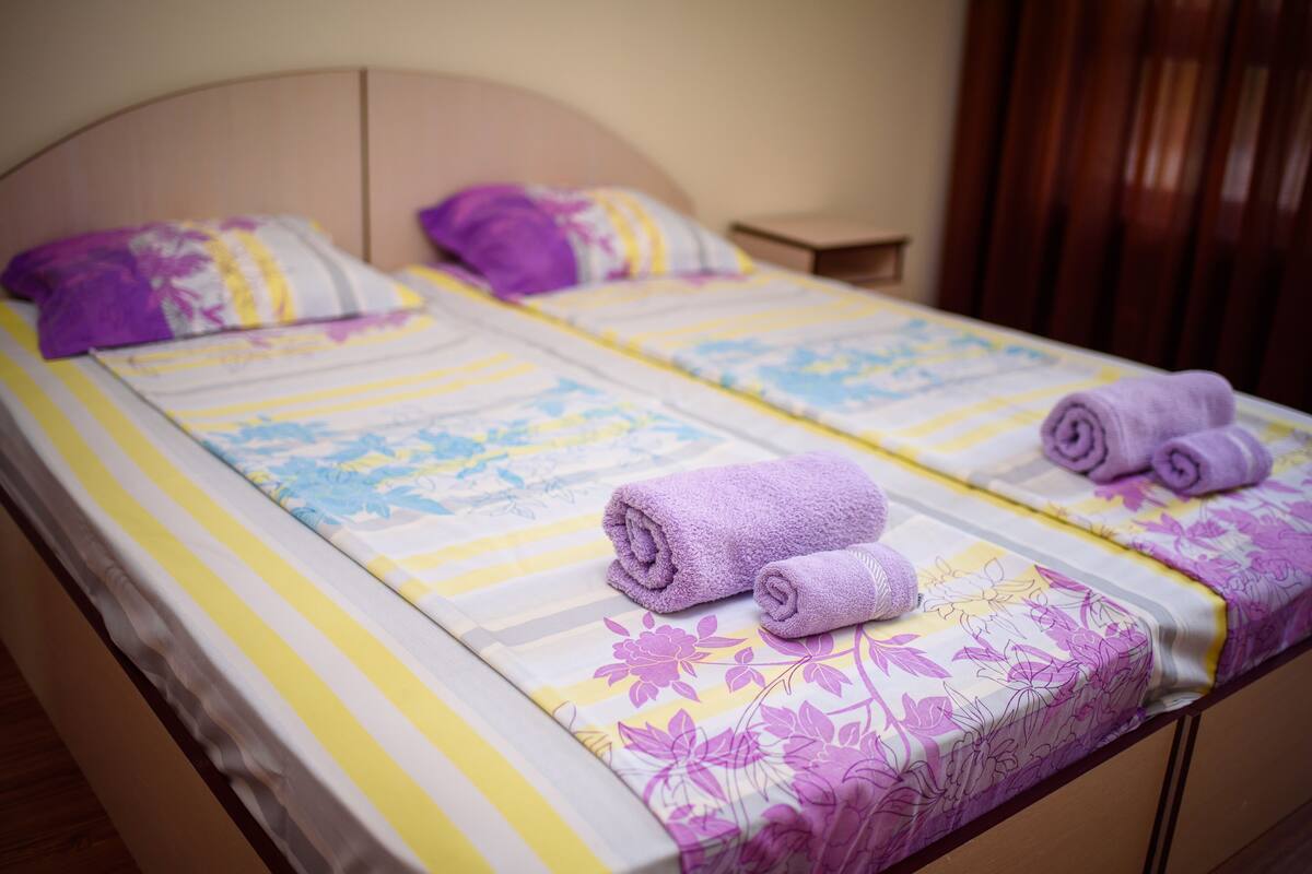 A double bed with floral bedding and two rolled towels.
