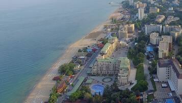 Vista aérea de una ciudad costera con playa, edificios de gran altura y una plaza central con piscina.