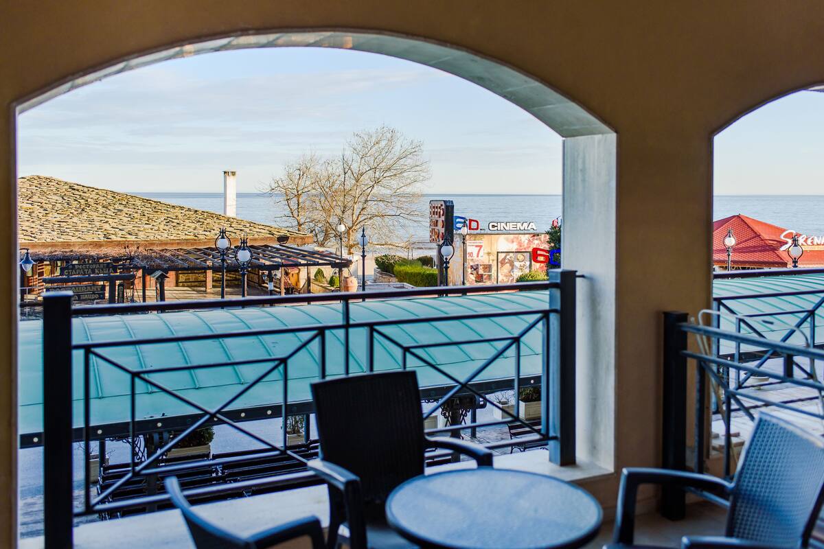 A balcony with chairs and tables, overlooking a beach and a cinema.