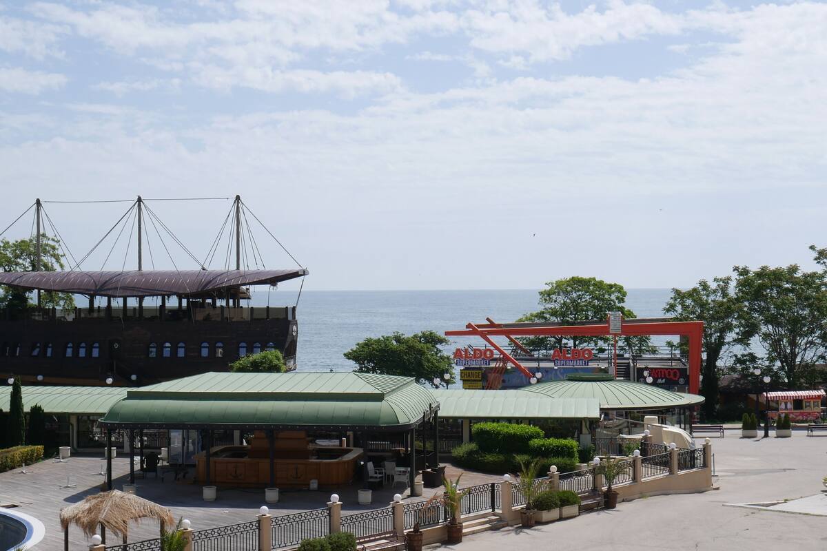 A waterfront area with a wooden boat structure, a covered seating area, and a supermarket.