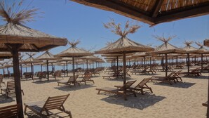 A beach with wooden lounge chairs and thatched umbrellas, arranged in rows. - Sea View Rental Front Beach (Golden Sands)