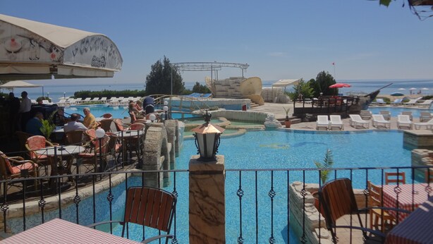 A poolside area with lounge chairs, tables, and a view of the sea. - Sea View Rental Front Beach (Golden Sands)