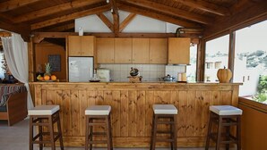 A kitchen with wooden cabinets, a white refrigerator, and a bar area with stools. - Dora Apartments (Malevizi)