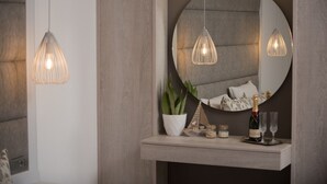 A modern interior with a round mirror, pendant lights, a potted plant, decorative items, and a bottle of champagne on a shelf. - Dora Apartments (Malevizi)