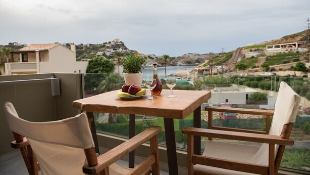 A balcony with a table set for two, overlooking a coastal landscape with buildings and greenery. - Dora Apartments (Malevizi)