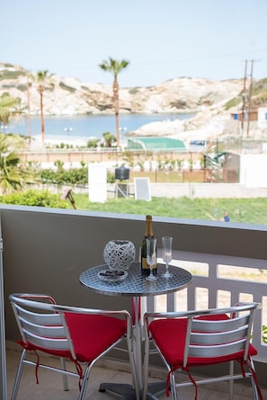 Un balcón con mesa y sillas, con vistas a una costa rocosa con palmeras.