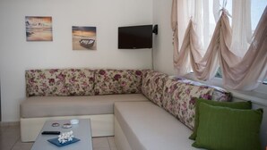 A modern living room with a sofa, a flat-screen TV, and a window with curtains. - Dora Apartments (Malevizi)