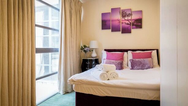Ein Hotelzimmer mit einem großen Bett, einem Nachttisch mit Lampe und einem Fenster mit Vorhängen.