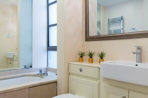 A bathroom with a large mirror, a sink, a towel rack, and two potted plants on the vanity. - Spacious 2-bedroom Apartment in Mayfair (London)