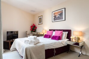 A hotel room with a large bed, a TV, a bedside table with a lamp, and a picture on the wall. - Spacious 2-bedroom Apartment in Mayfair (London)