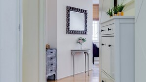 Ein Flur mit Holzboden, einem weißen Schminktisch, einem kleinen Tisch mit einer Vase und einem dekorativen Spiegel an der Wand.