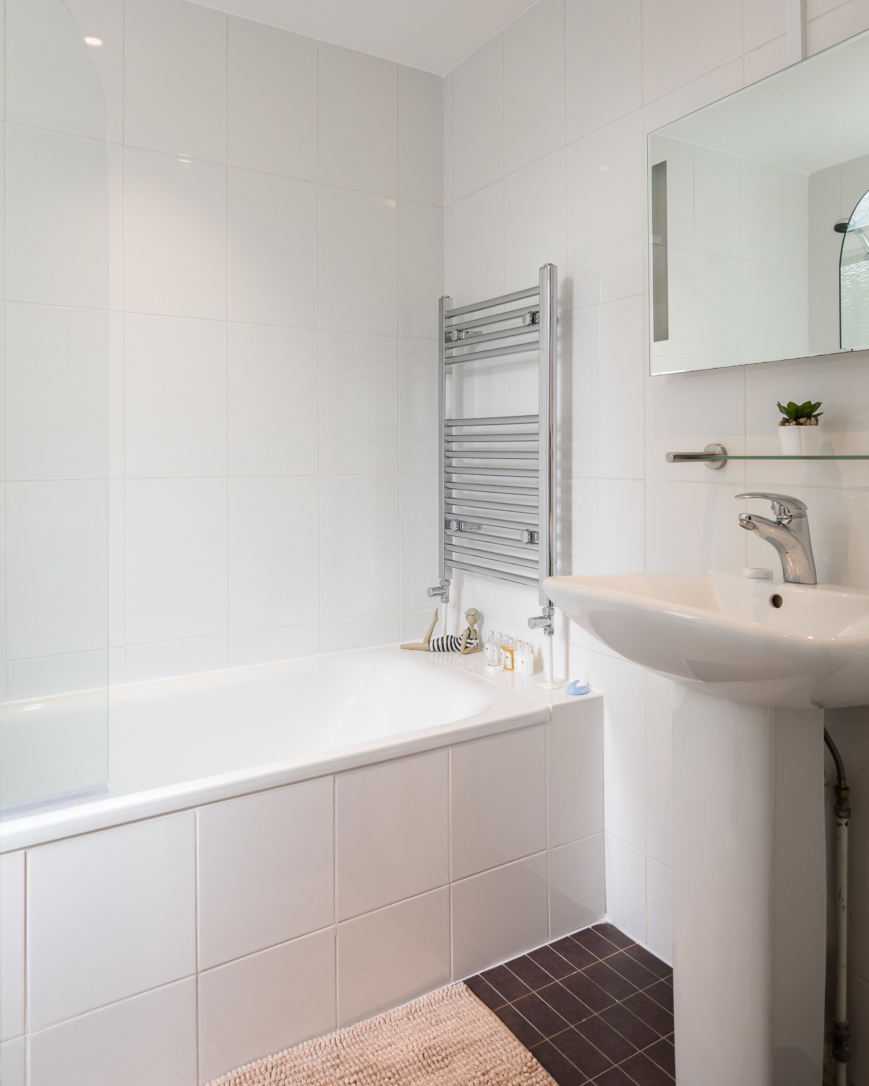 A modern bathroom with a white bathtub, a glass shelf above the sink, and a small potted plant on the shelf.