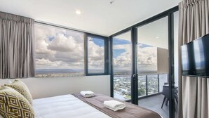 A hotel room with a large bed, a TV, and a balcony with a city view. - Luxurious 2 Bedroom Brand New Apartment With Amazing Hinterland Views (Broadbeach)