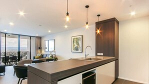 A modern kitchen with a central island, a dining area with a view, and a large window. - Luxurious 2 Bedroom Brand New Apartment With Amazing Hinterland Views (Broadbeach)