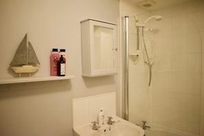 Une salle de bain équipée d’un lavabo, d’un miroir, d’une douche et d’une étagère où sont rangés les articles de toilette.