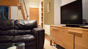 A living room with a black leather sofa, wooden cabinet, and a large flat-screen TV. - Minimal Studio With Views Over Battersea Park (London)
